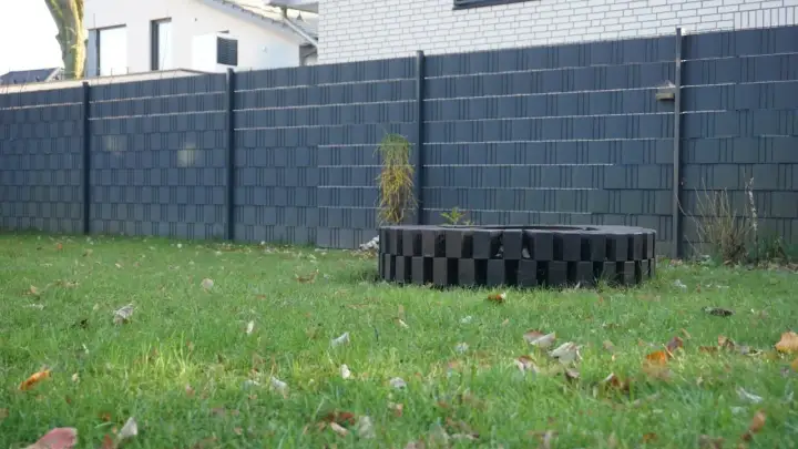 Moderne Zaun-Sichtschutz-Ideen: Dunkelgrauer Lamellenzaun mit dekorativem Feuerring im Garten.